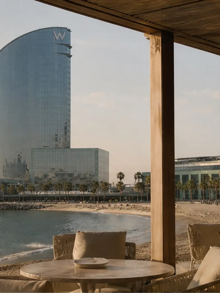 W Barcelona sail hotel and covered coastal terrace at soft golden hour, quiet-luxury Plan B proposal mood