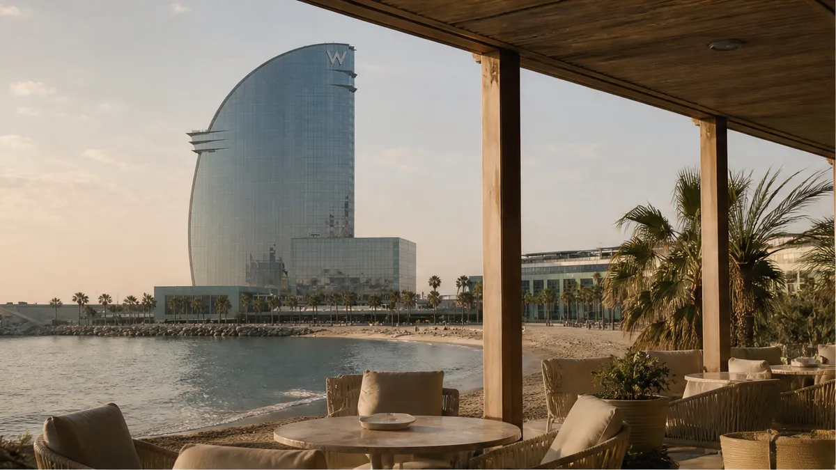 W Barcelona sail hotel and covered coastal terrace at soft golden hour, quiet-luxury Plan B proposal mood